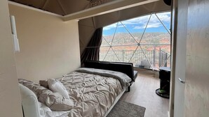 A bedroom with a bed, a window, and a view of a red landscape.