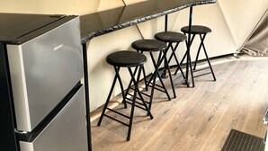 A compact kitchenette with a stainless steel refrigerator, a black countertop, and three black stools.
