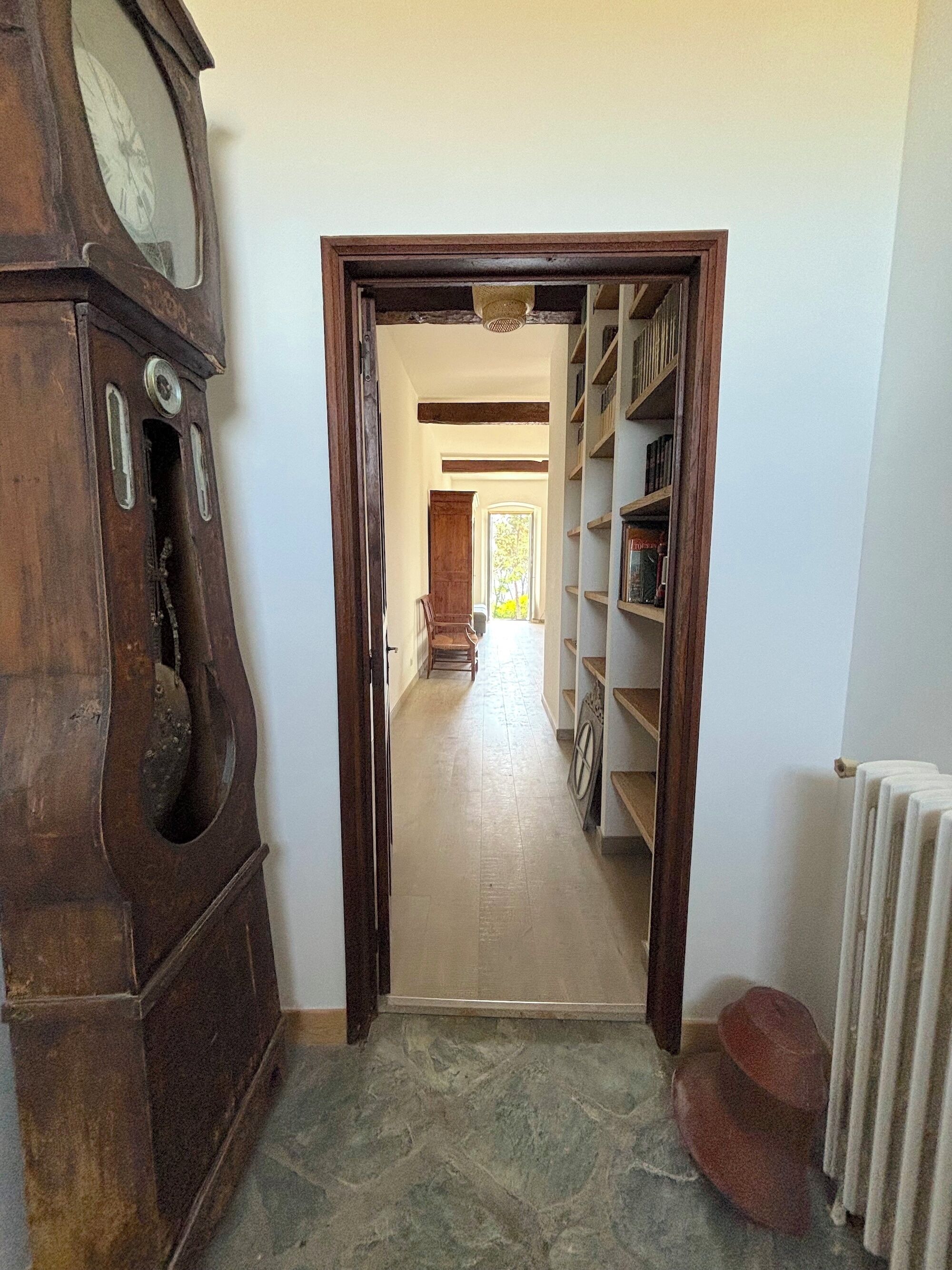 Un couloir avec une porte en bois donnant sur une pièce équipée d’un radiateur et d’une chaise.