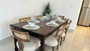 Una mesa de comedor dispuesta con platos, tazones y copas de vino, rodeada de sillas con asientos acolchados.