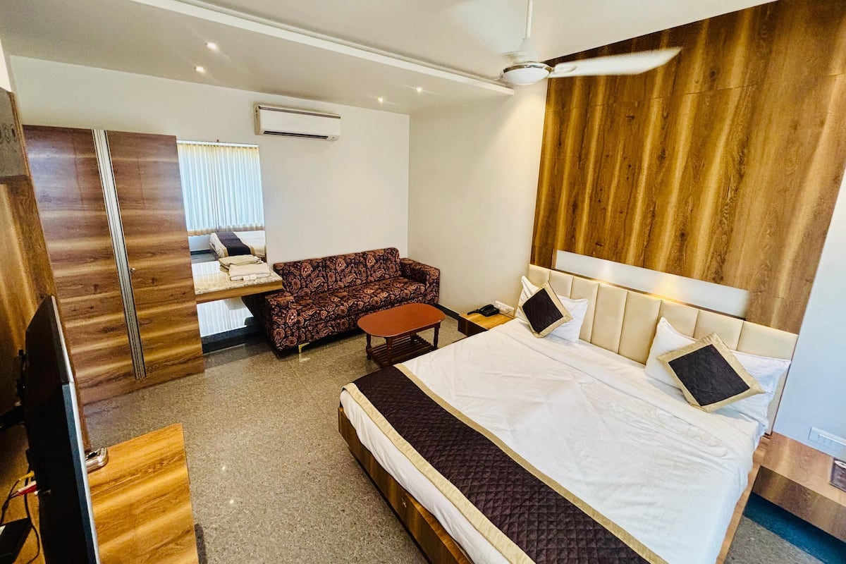 A hotel room with a bed, a sofa, a TV, and a ceiling fan.