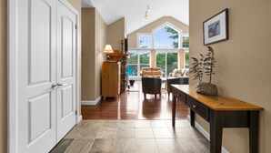A spacious hallway with a wooden floor, a stone fireplace, and a view of the outdoors through large windows.