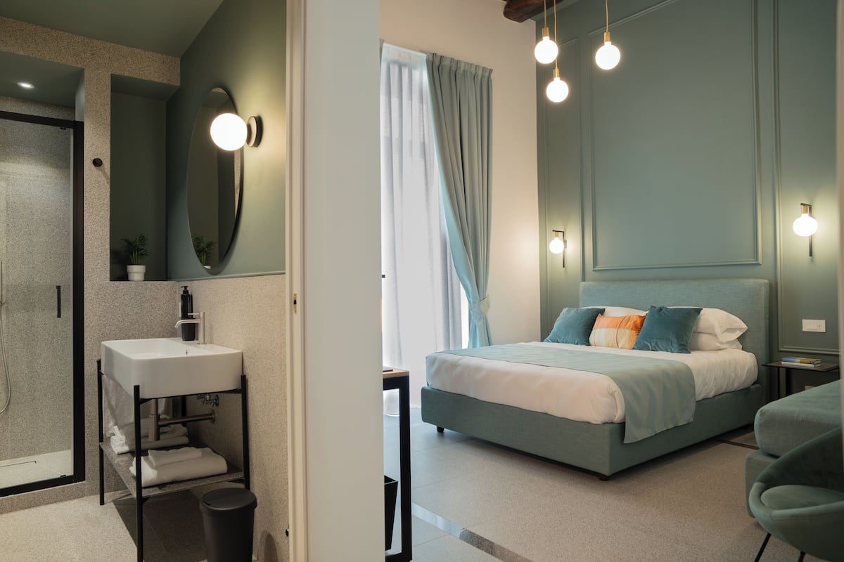 Un dormitorio moderno con cama, mesita de noche y baño con lavabo y espejo.