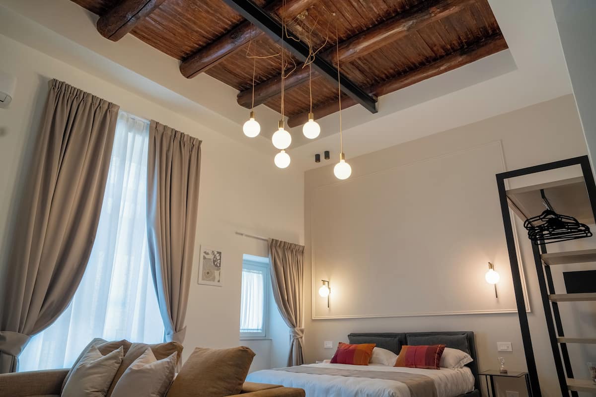 Un dormitorio con cama, sofá, techo de madera y una lámpara fijada a la pared.