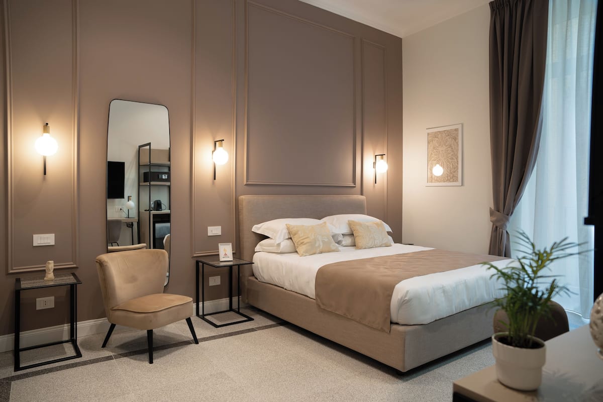 Una habitación de hotel moderna con una cama grande, una silla, una mesita y un espejo.