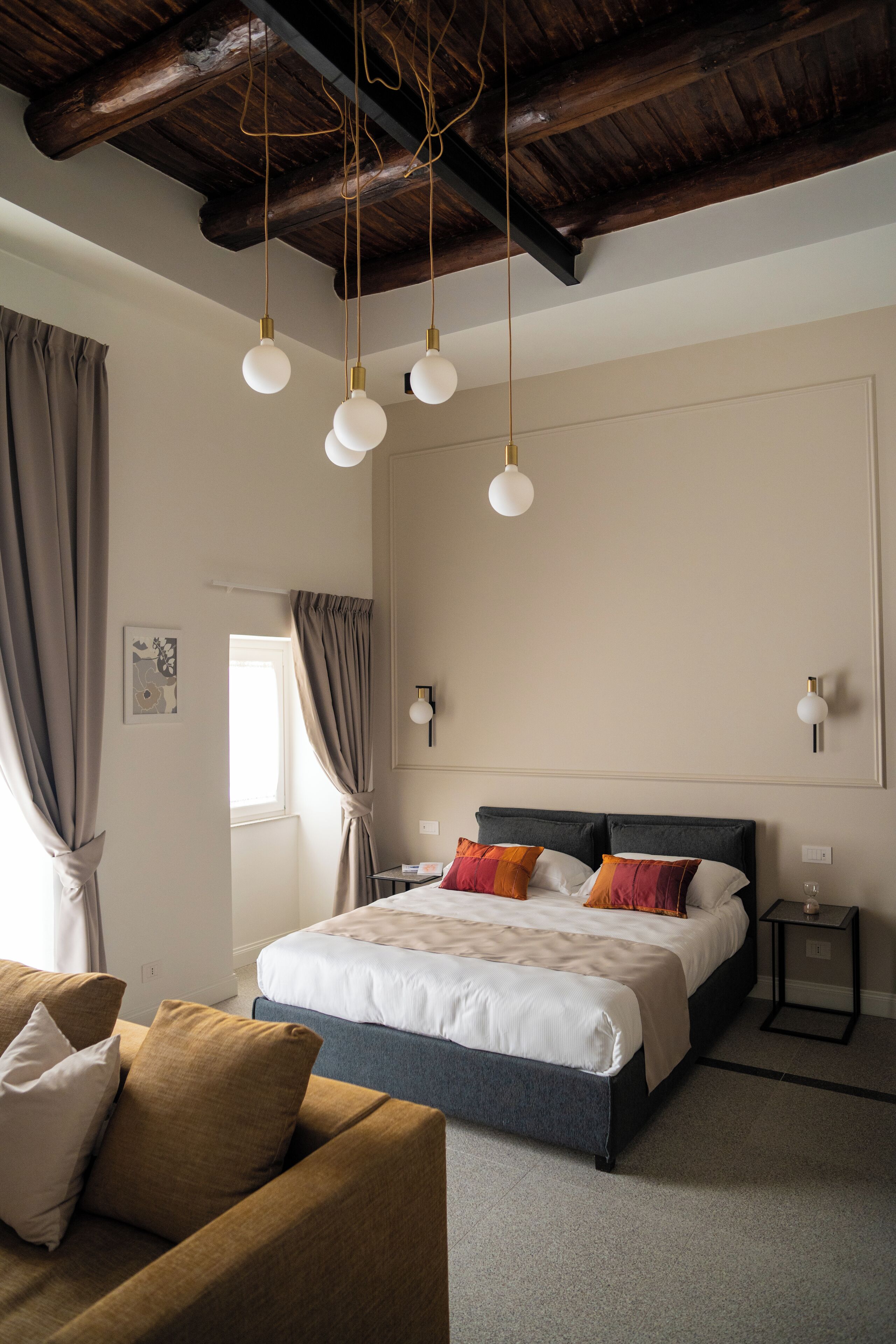 A bedroom with a bed, a nightstand, a sofa, and a ceiling with exposed beams.