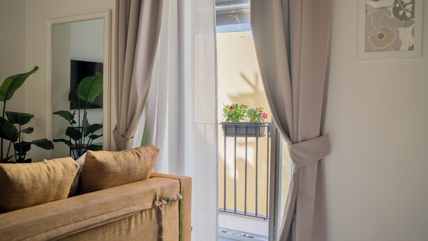 A room with a beige sofa, a mirror, a potted plant, and a balcony with a railing. - Monteroduni 22 - Chiaia Design Rooms (Naples)