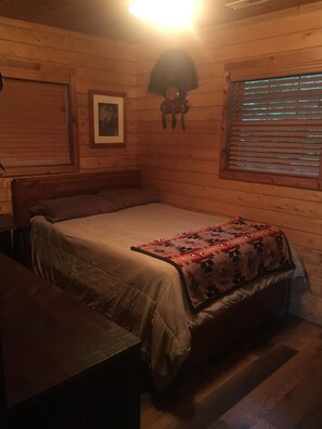Une chambre dans un chalet en bois, avec un lit, un bureau et une fenêtre équipée de stores.