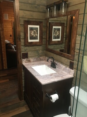 Une salle de bain avec un lavabo en marbre, des meubles en bois, un miroir et des œuvres d’art florales encadrées accrochées au mur.