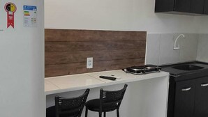 A compact kitchen with a white countertop, two black bar stools, a black sink, and a refrigerator with a red sticker. - APARTMENT ACONCHEGO, NEXT TO NORTH SHOPPING AND DOWNTOWN MARACANAU (Jereissati II Maracanaú)