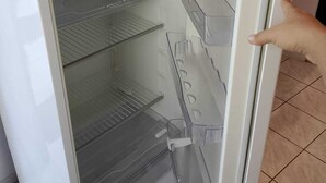 An open refrigerator with clear shelves and a hand pointing to the door. - APARTMENT ACONCHEGO, NEXT TO NORTH SHOPPING AND DOWNTOWN MARACANAU (Jereissati II Maracanaú)