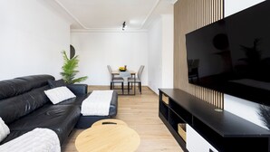Ein modernes Wohnzimmer mit einer schwarzen Ledersofa, einem Holztisch, einem Flachbildfernseher und einem Essbereich mit Tisch und Stühlen.