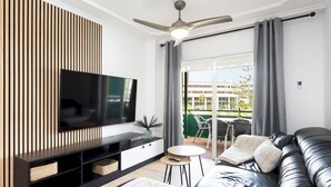 Ein modernes Wohnzimmer mit Flachbildfernseher, Deckenventilator und einem Balkon mit Blick auf ein Gebäude.