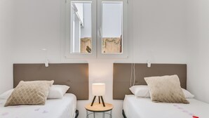 Een hotelkamer met twee bedden, een klein tafeltje met een lamp en een raam met uitzicht op het strand.