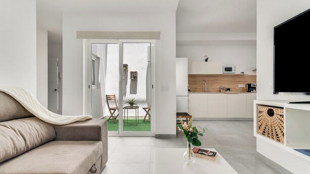 Een moderne woonkamer met een bank, een bijzettafeltje met een vaas, en een keukenhoek met een televisie en kasten.