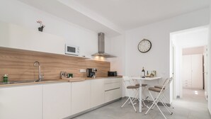 Een moderne keuken met een houten aanrecht, een ingebouwde magnetron en een roestvrijstalen afzuigkap. Er is een zithoek met een kleine tafel en stoelen.