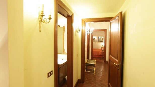 A narrow hallway with a wooden door on the right, a small bench, and a mirror on the left.