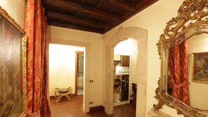 A hallway with a wooden ceiling, a mirror with an ornate frame, and a door leading to a kitchen area.