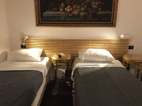 Habitación de hotel con dos camas, un cuadro de frutas en la pared y una pequeña mesa redonda entre las camas.