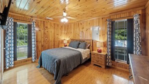 Un dormitorio con paneles de madera, una cama, mesitas de noche y un ventilador de techo.
