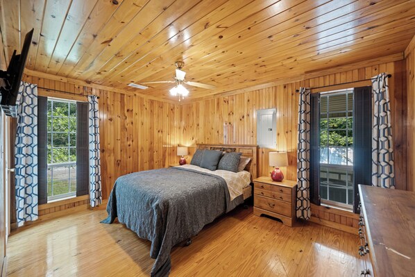 Ein Schlafzimmer mit Holzwänden, einem Bett, Nachttischen und einem Deckenventilator.
