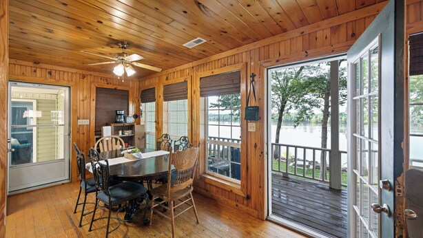 Un interior de madera con comedor, ventilador de techo y amplias ventanas con vistas a un lago.