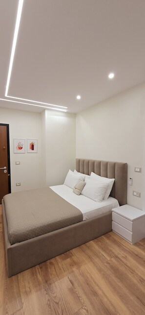 A modern bedroom with a large bed, bedside tables, and a door. - Arkle Apartment 7 (Tirana)