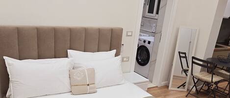 A bedroom with a large bed, a washing machine, and a dining area.