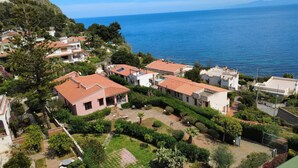 A coastal residential area with houses featuring red-tiled roofs, surrounded by lush greenery and a clear view of the sea. - Lighthouse Villa (Santa Flavia)