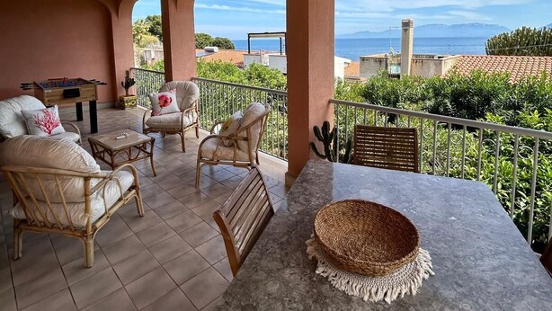 A covered outdoor seating area with wicker furniture, a foosball table, and a view of the sea. - Lighthouse Villa (Santa Flavia)