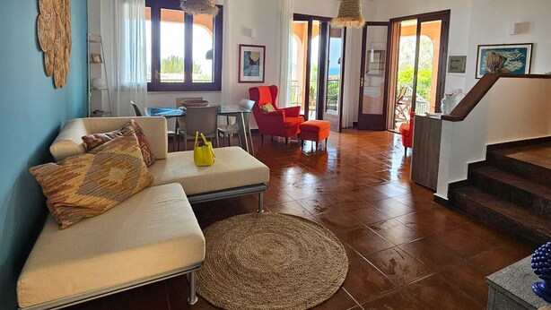 A spacious living area with a sofa, chairs, a round rug, and a staircase leading to another level. - Lighthouse Villa (Santa Flavia)