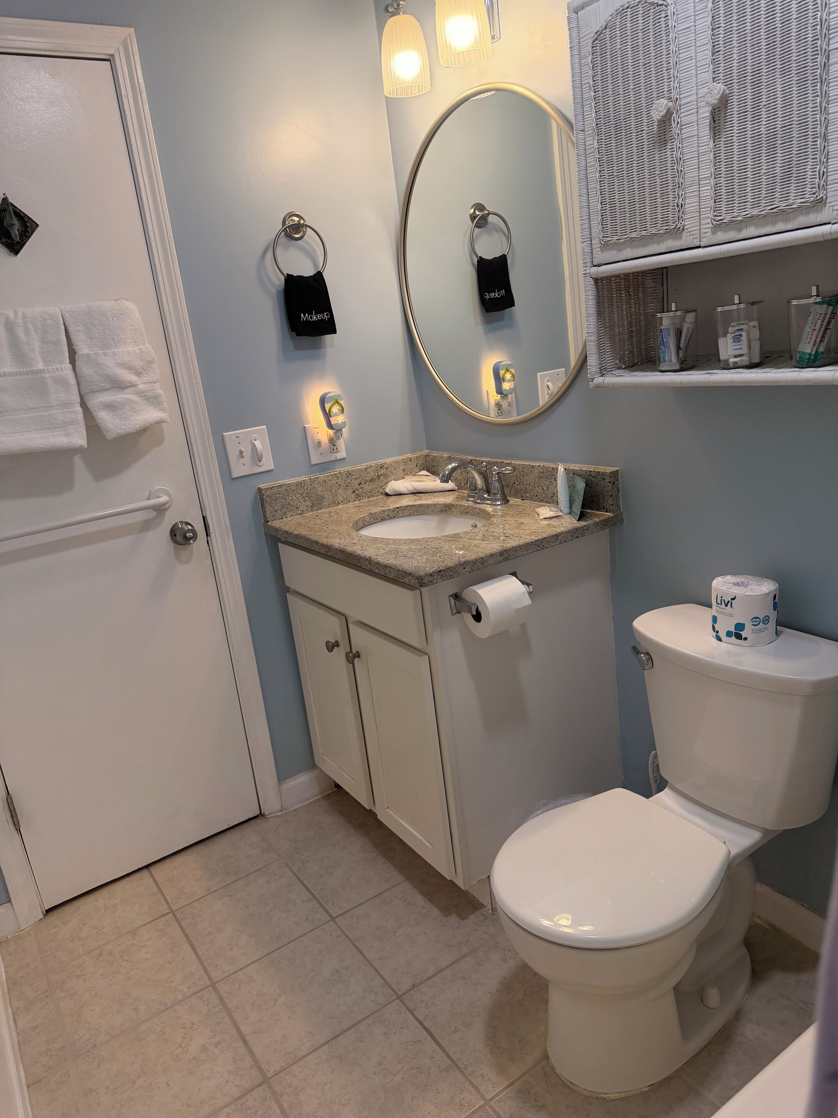 Ein Badezimmer mit Toilette, Waschbecken, Handtuch, Spiegel und Ablage mit Pflegeartikeln.
