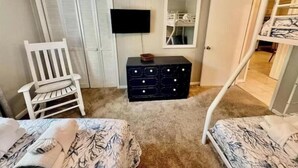 A bedroom with two beds, a white chair, a dresser, a TV, and a closet.