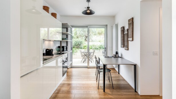 A modern kitchen with a wooden floor, white cabinets, and a dining area with a table and chairs.