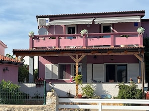 A two-story pink building with a balcony, a covered porch, and a satellite dish.
