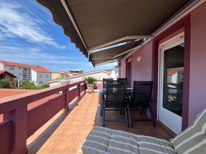 A balcony with a table and chairs, potted plants, and a view of neighboring buildings.