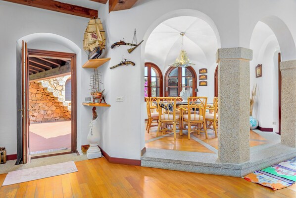A spacious dining area with wooden chairs and a table, surrounded by arched windows and a stone pillar.