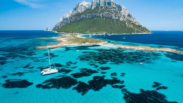 An aerial view of a coastal area with clear turquoise waters, a sailboat, and a prominent rocky island with a peak. - Exclusive villa with pool and sea view in Puntaldia ( San Teodoro) (Puntaldia)