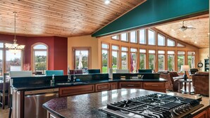 Una cocina amplia con una isla grande, techo de madera y ventanas grandes que ofrecen vistas al exterior.