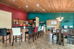 Una cocina amplia con armarios de madera y una pared de acento roja, una zona de bar con taburetes y una mesa de comedor con sillas.