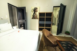 A hotel room with a bed, a brown armchair, a wooden wardrobe, and a door leading to a bathroom. - The Big Blue Resort & Spa (Nyanyanu)