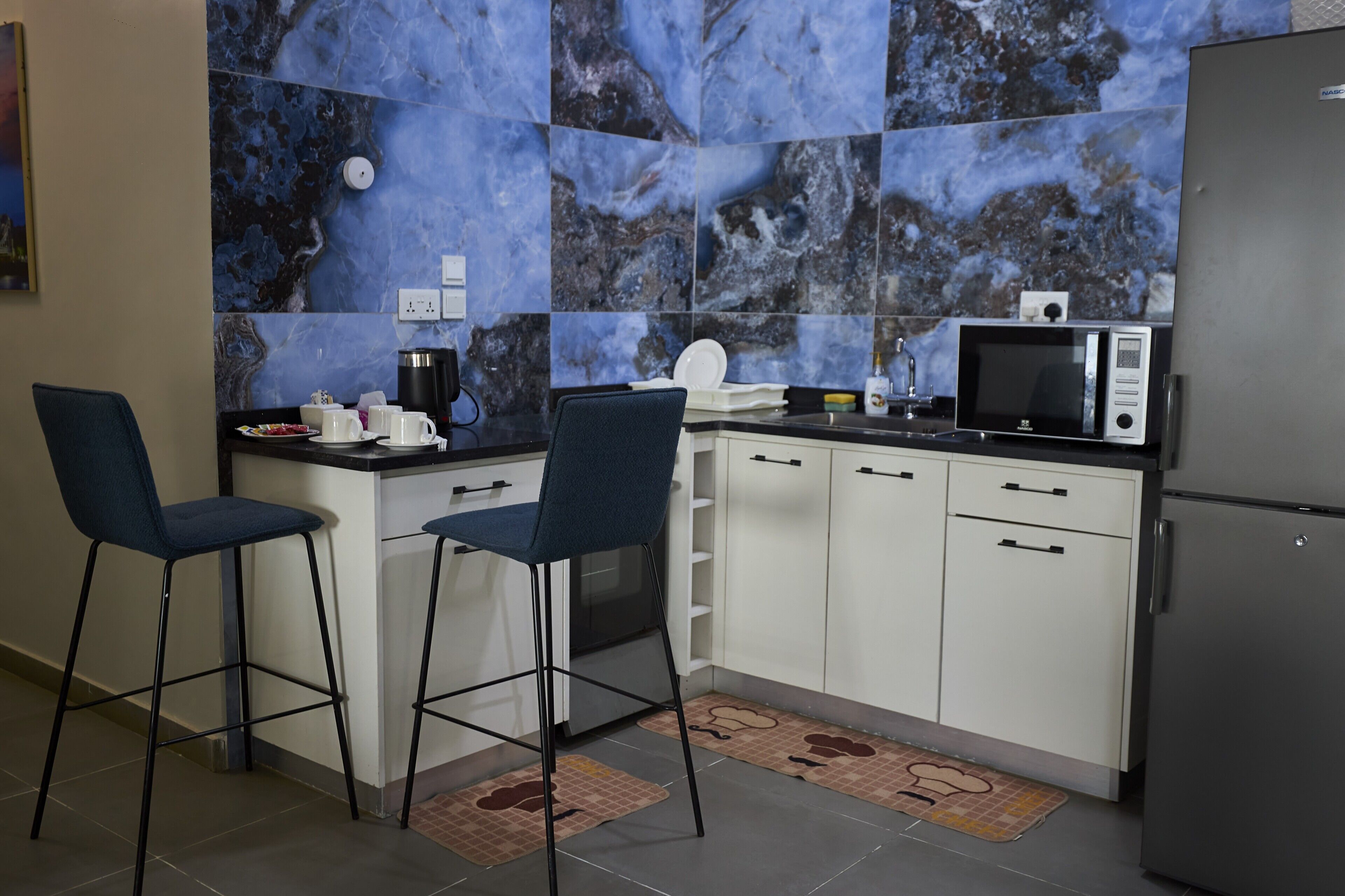 A compact kitchen with white cabinets, a black refrigerator, a microwave, and two bar stools.