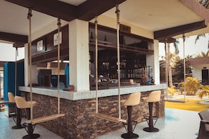 A bar area with a stone counter, bar stools, and a swing seating area. - The Big Blue Resort & Spa (Nyanyanu)