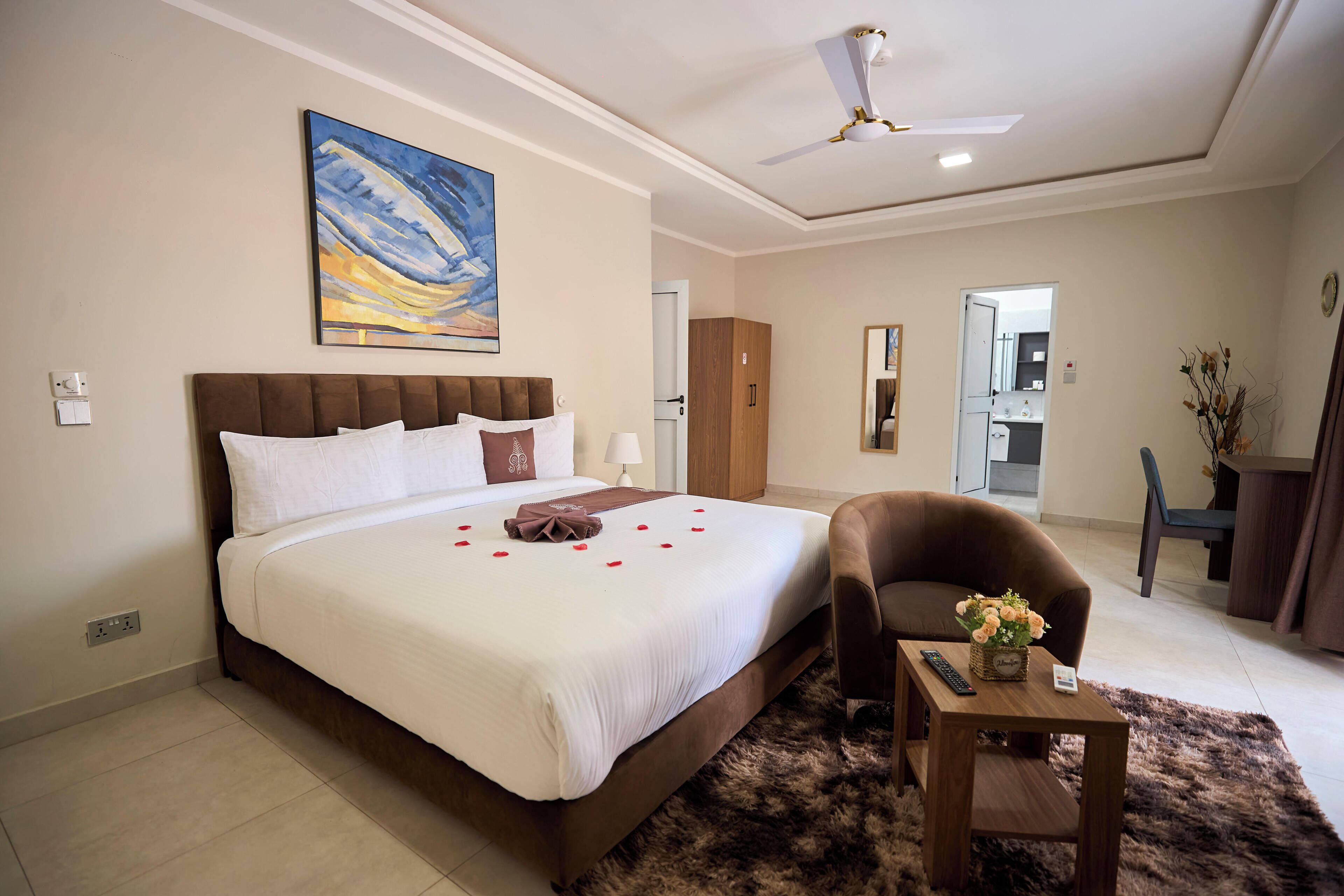 Habitación de hotel con una cama grande, una silla, una mesita y un cuadro en la pared.