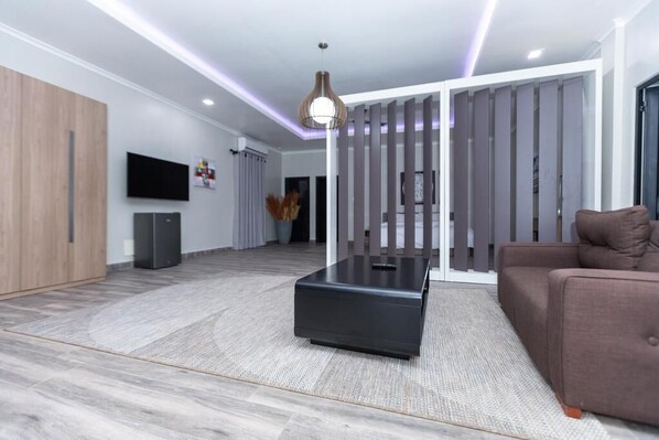 A modern living room with a flat-screen TV, a black coffee table, a brown sofa, and a decorative light fixture. - The Big Blue Resort & Spa (Nyanyanu)