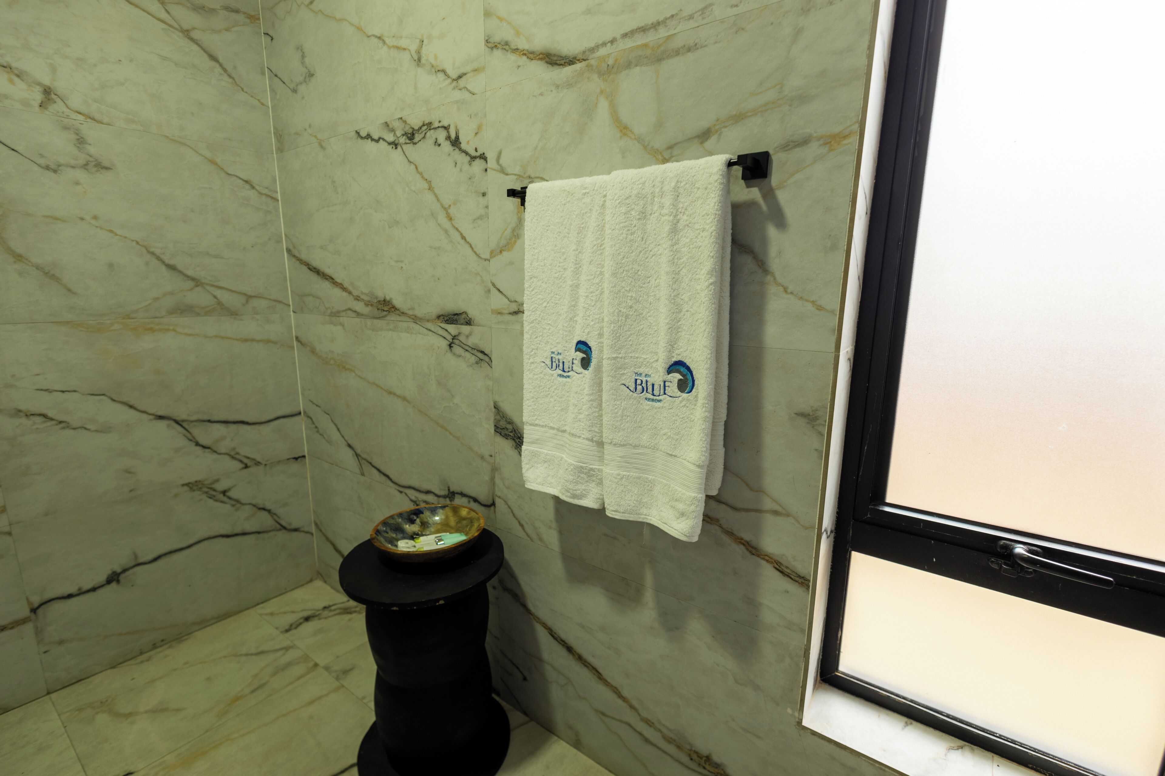 A bathroom with marble walls, a toilet, a sink with a bowl, and a towel hanging on a rack.