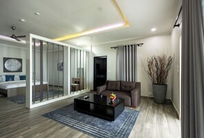Una sala de estar moderna con un sofá, una mesa de centro, un televisor y un ventanal corredera que da a un dormitorio.
