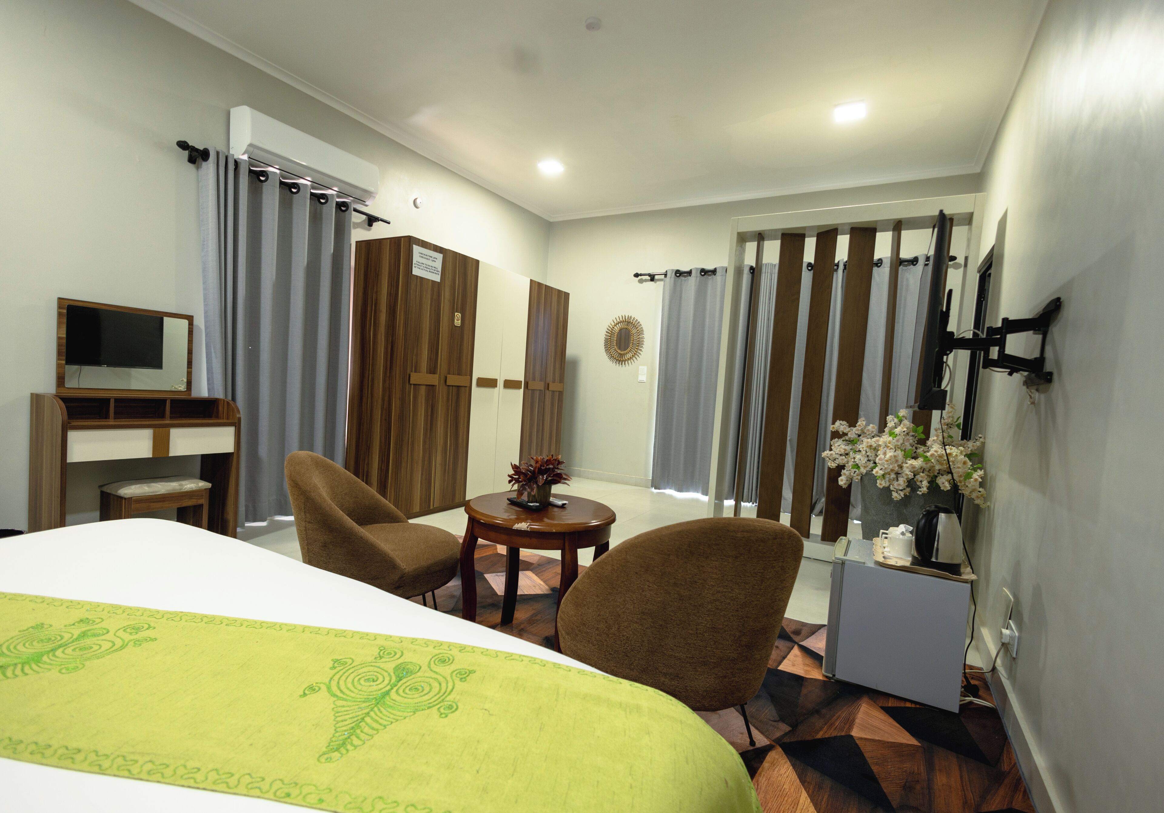 A hotel room with a bed, two chairs, a small table, a TV, and a window with curtains.