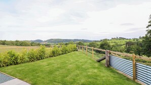 A well-maintained lawn with a wooden fence and metal railing, offering a view of rolling hills and fields. - Charollais (Oswestry)