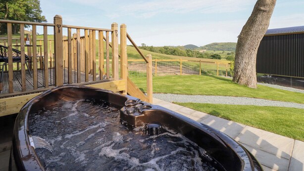Ein Whirlpool auf einer Holterrasse mit Blick auf eine grüne Landschaft und Hügel.